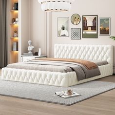 a white bed sitting on top of a wooden floor next to a wall with pictures above it