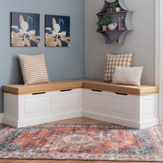 a corner bench with two pillows on it in front of a blue wall and rug