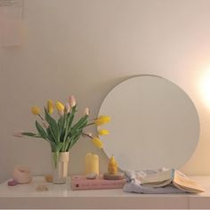 a vase with yellow tulips sitting on a table next to a round mirror