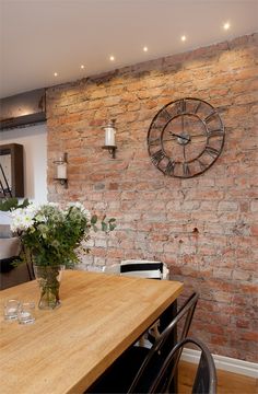 a wooden table sitting in front of a brick wall with a clock on it's face