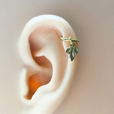 a pair of ear piercings with green leaves on them sitting on top of a white surface