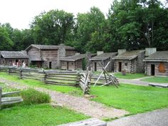 an old log cabin in the woods with people walking around