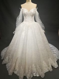 a white wedding dress with long sleeves and lace on the skirt is displayed in front of a mannequin