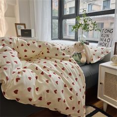 a bed with hearts on it in front of a window and a stuffed animal next to it