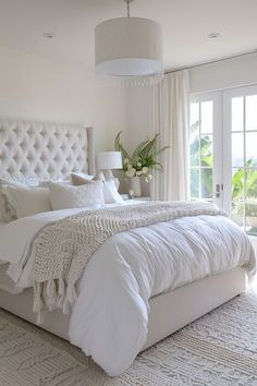 a large white bed sitting in a bedroom next to a window covered with curtains and pillows