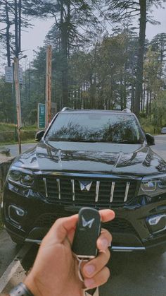 a hand holding a car key in front of a black suv parked on the street