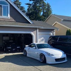 a white sports car parked in front of a garage with two black cars next to it