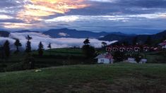 the clouds are rolling in over the mountains and houses on the hill side at dusk