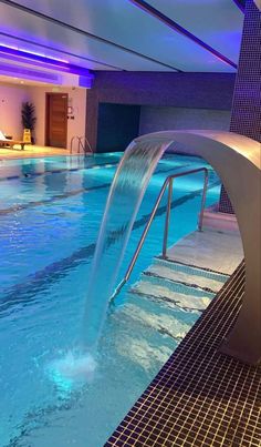 an indoor swimming pool with blue lights and water features a waterfall running down the side