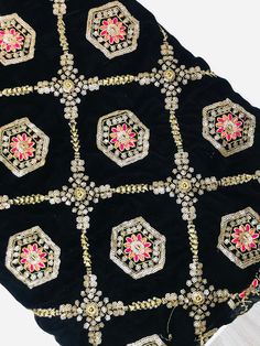 an embroidered black and gold cloth with pink flowers on the center, surrounded by beads