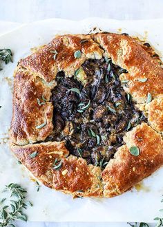 an artisan bread with mushrooms and herbs in it on a white platter surrounded by greenery