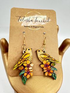 a pair of yellow bird earrings with flowers on them sitting on top of a wooden stand