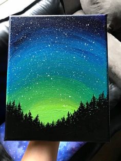 someone is holding up a painting with the stars in the night sky and trees on it