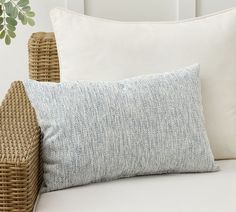 a close up of a pillow on a bed next to a wicker basket and plant