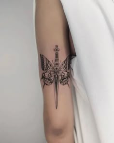 a black and white photo of a butterfly with a dagger tattoo on the left arm