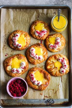 baked pastries with butter and raspberries on a baking sheet next to a cup of orange juice