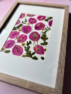 an art work with pink flowers and green leaves on white paper in a wooden frame