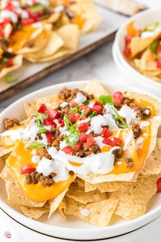 two plates filled with nachos topped with cheese and toppings next to tortilla chips