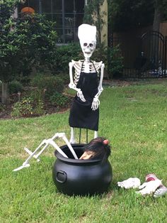 a fake skeleton sitting on top of a black pot in the middle of a yard