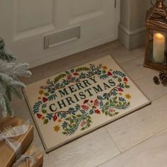 a merry christmas door mat on the floor next to presents and a lit up candle