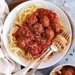 spaghetti and meatballs are served on a white plate with a red striped towel next to it