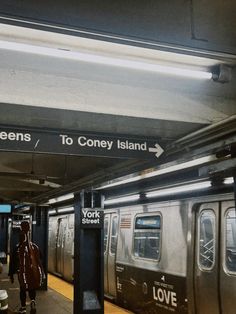 two people are walking on the platform near a subway car and sign that says to coney island