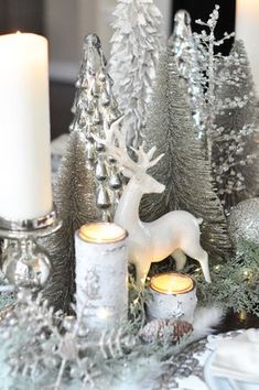 a table topped with candles and christmas trees covered in snow next to a white deer