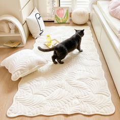 a black cat standing on top of a white rug next to pillows and bookshelves