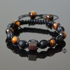 "Adjustable and trendy, you will never want to take this gemstone beaded bracelet off. Featuring a Hematite cube as its centerpiece, this beaded bracelet is made with natural 8 mm Tigers Eye and matte Black Onyx beads. This piece of mens jewelry is strung on a waxed cord and finishes off with an adjustable closure adorned with two Tigers Eye stopper beads. Hematite is said to stimulate mental activity, balance yin and yang energies and dissolve negative energies. It is considered a grounding and Two Tigers, Bracelet Christmas, Tigers Eye Necklace, Hematite Bracelet, Bracelet Mens, Healing Crystal Jewelry, Bracelet Crystal, Christmas Bracelet, Jewelry Beaded