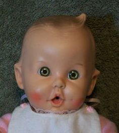 an old baby doll with big eyes laying on the floor looking at the camera while wearing a bib