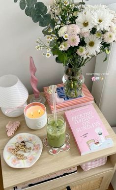 a wooden table topped with a vase filled with flowers next to a book and candle