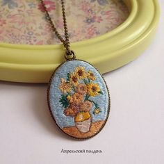 an embroidered necklace with flowers in a vase on the front and back side, hanging from a gold chain