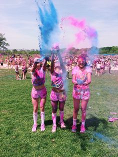 two women in pink and blue paint throwing colored powder at each other on the grass