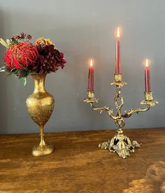 a gold candelabra with three candles and flowers in it on a wooden table