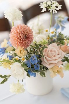 a white vase filled with lots of flowers on top of a table covered in blue and white napkins