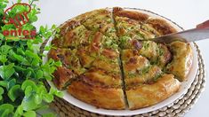 a person cutting into a pizza on top of a white plate next to green plants