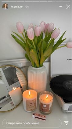 a vase filled with pink tulips next to a record player and candle holders