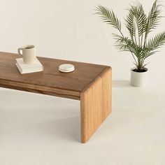 a wooden table with a cup and saucer on it next to a potted plant