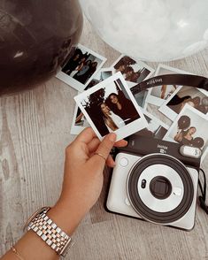 a person holding an old camera with polaroid pictures on the table next to it