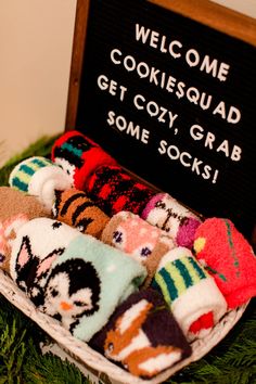 a basket filled with lots of colorful socks next to a sign that says welcome cookiesquaad get cozy grab some socks