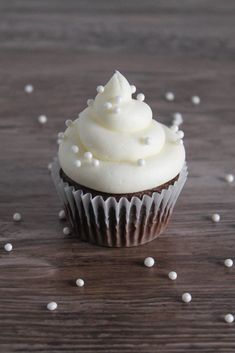 a cupcake with white frosting and sprinkles on a wooden table