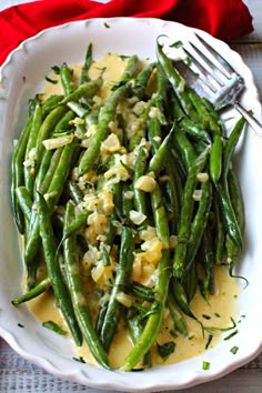 a white plate topped with green beans covered in gravy next to a fork