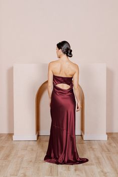 a woman in a red dress standing on a wooden floor with her back to the camera