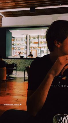 a woman sitting at a table with a glass in her hand and looking off into the distance