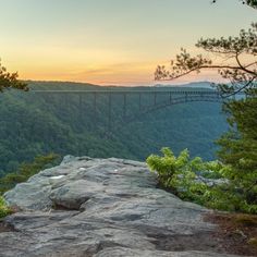 the sun is setting over mountains and trees with a bridge in the distance above it