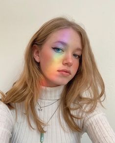 a woman with long blonde hair and blue eyes wearing a white turtle neck sweater is looking at the camera