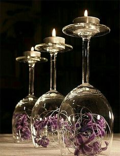 three wine glasses with purple flowers in them and one has a candle on the top