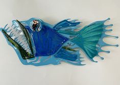 a blue glass fish sculpture sitting on top of a white table next to a wall