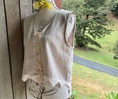 a white top with an embroidered flower on it hanging from a wooden wall next to grass and trees