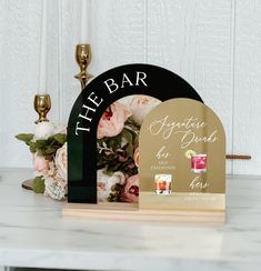 a wedding guest book and plaque on a marble table with flowers in the background, next to a candle holder